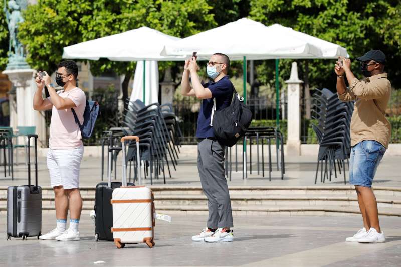 Tres turistas cargados con sus maletas realizan una foto en la plaza de la Virgen de ValÃ¨ncia.