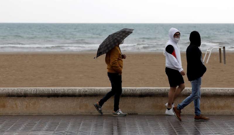 Un grupo de personas pasea cerca de la playa en un día lluvioso.