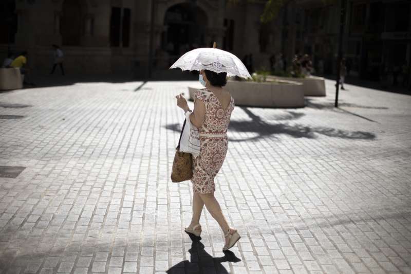 Una mujer se protege del intenso calor en una calle del centro histórico de Valencia. La Conselleria de Sanidad ha declarado el nivel de alerta sanitaria por ola de calor alto en municipios de seis comarcas de la Comunitat Valenciana. EFE/Biel Aliño
