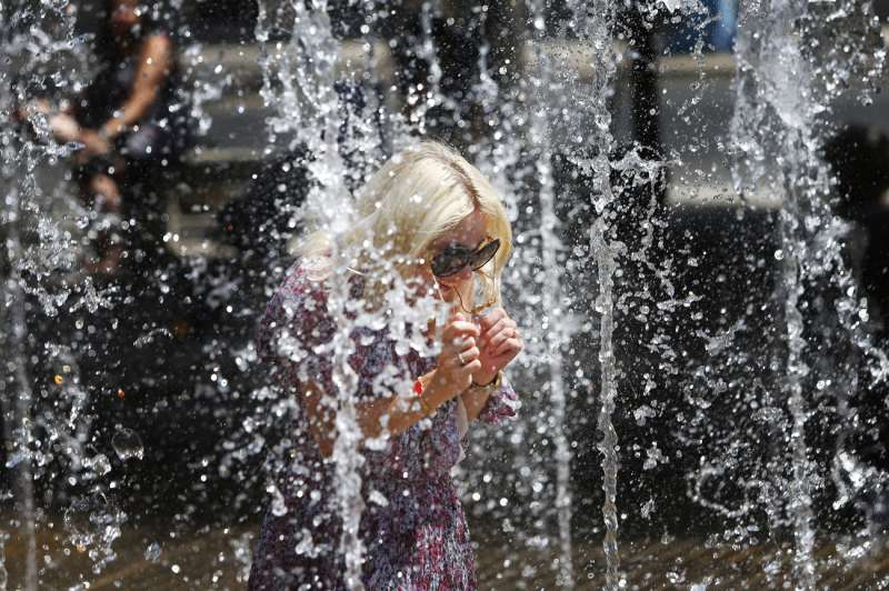 Una mujer mitiga el calor en los chorros de una fuente. /EFE
