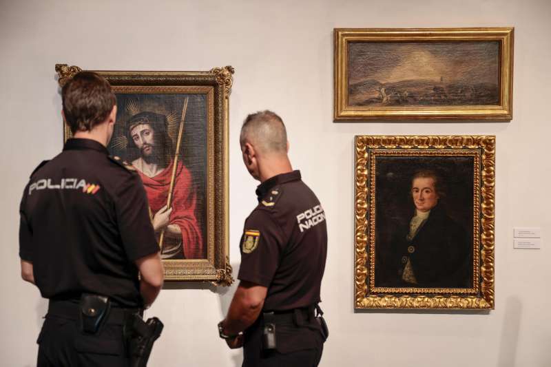 Dos agentes de la unidad de la Policía Nacional adscrita a la Comunitat Valenciana contemplan tres de las cinco obras de arte falsas que eran atribuidas a Goya, Juan de Juanes y Renoir y que han incautado en una operación de la que han dado cuenta este jueves. /EFE