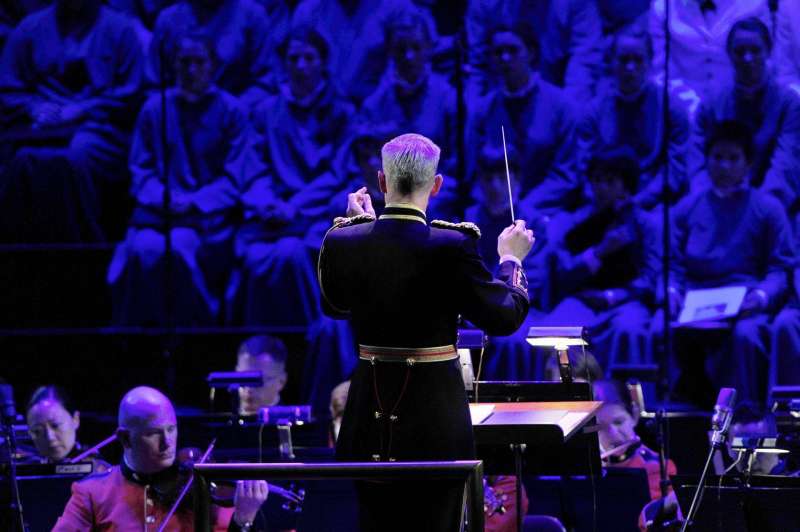 Imagen de un director de orquesta junto a un coro y una orquesta.
