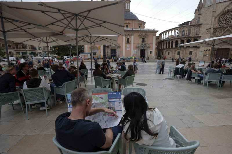 En la imagen, dos turistas consultan un mapa de la ciudad sentados en una terraza en la plaza de la Virgen, ocupada en su totalidad por visitantes extranjeros, en una imagen reciente. /EFE
