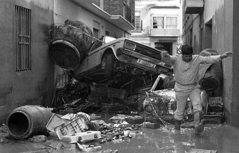 Espectacular imagen del 23/10/1982 de una calle de Alzira taponada por coches, mientras un vecino intenta llegar a su domicilio.