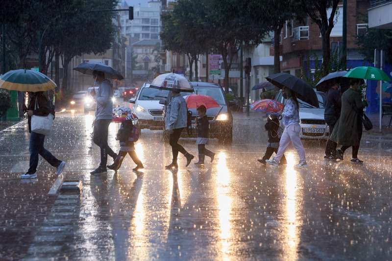 Varias personas cruzan una calle bajo la lluvia