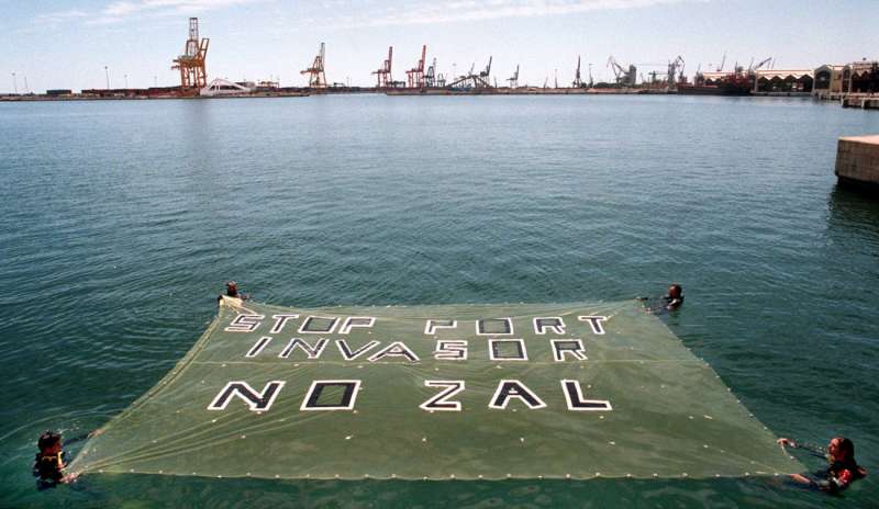 Un grupo de activistas despliegan una pancarta en protesta por la ampliación del puerto hacia la huerta. /EFE