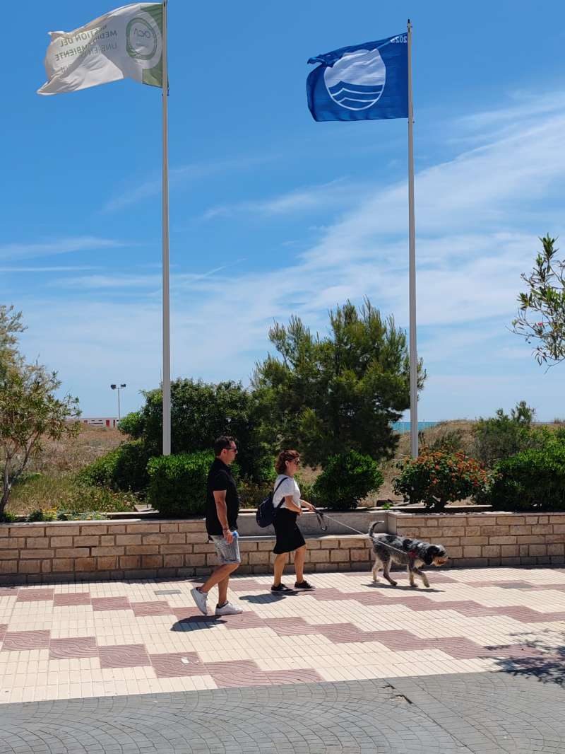 Paseantes, junto a una bandera azul en Canet.  EPDA